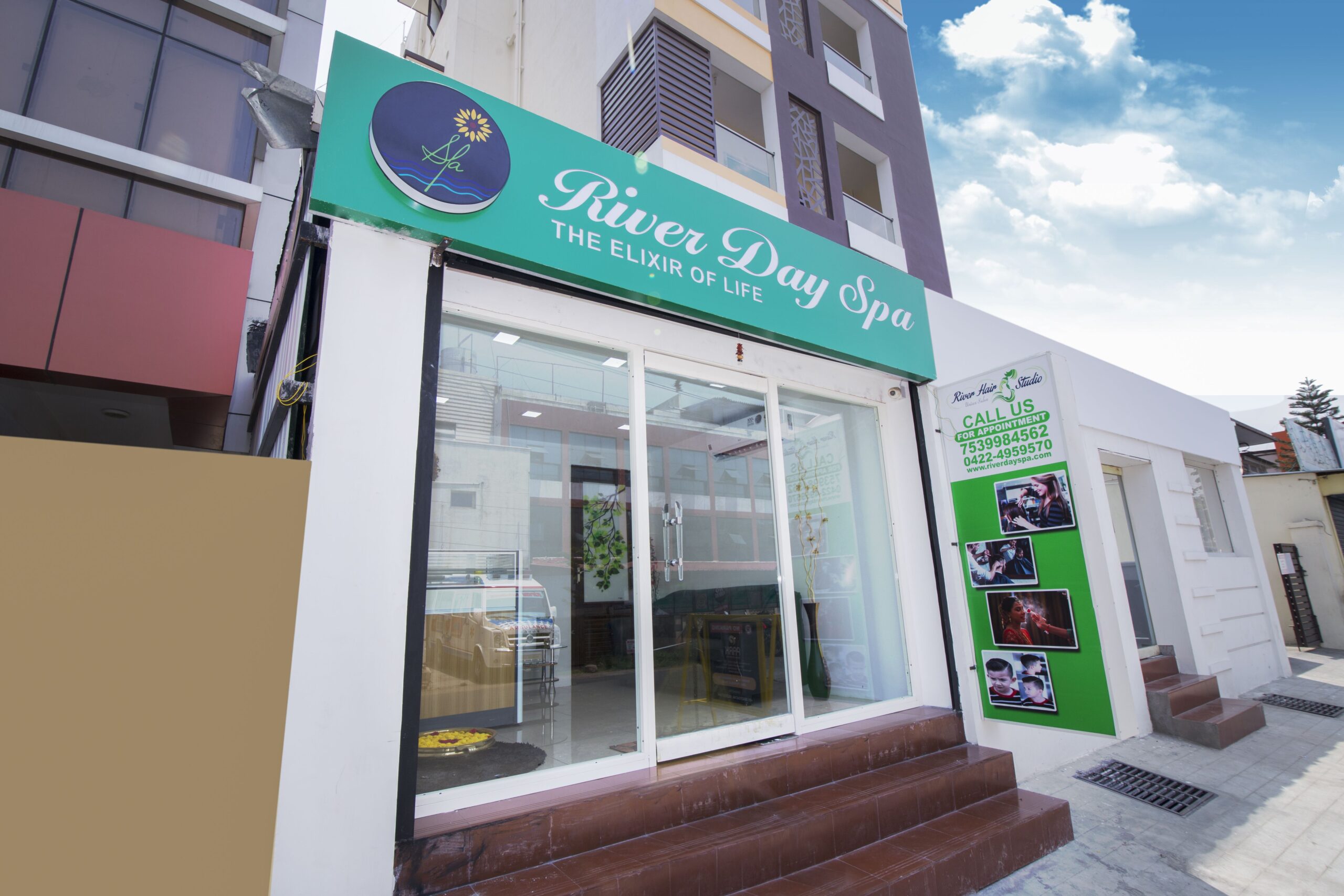 The River Day Spa building's front view features a front glass door and a vertical banner advertising their services, along with a contact number and a LED logo and signboard.