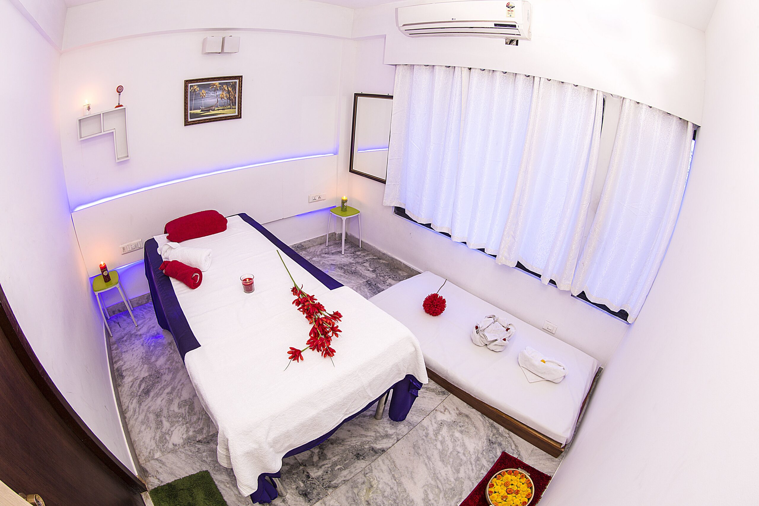 A top view of the fully air-conditioned room in the spa. Neatly arranged beds with the cot and floor bed at the side with pillow and towels rolled on into it. Lit up aromatic candles are placed at the corner of the rooms to improve the freshness of the saloon.
