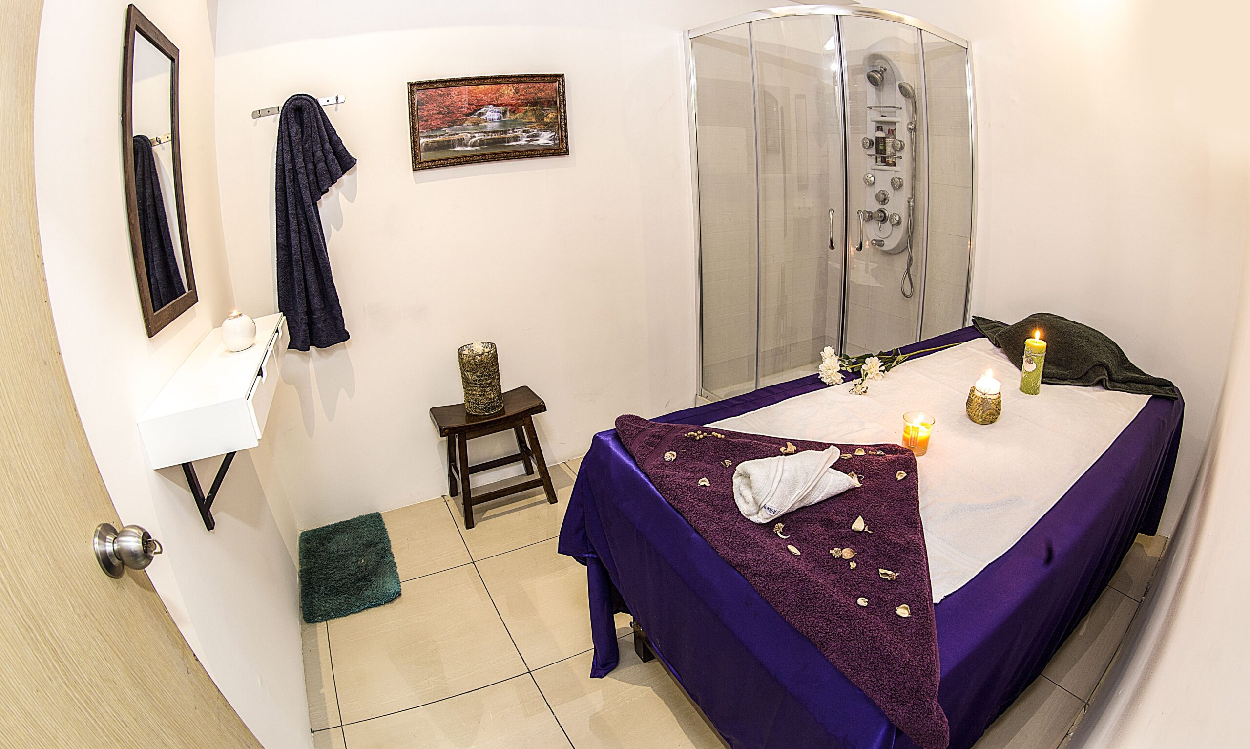 A Full view of the spa room with a beautifully decorated bed with fresh flowers and aromatic candles. A separate shower room is attached near the bed for customers convenience.