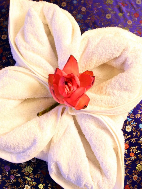 A lotus flower is held on the massage towel, both kept on a fluffy bed sheet at the professional massage centre
