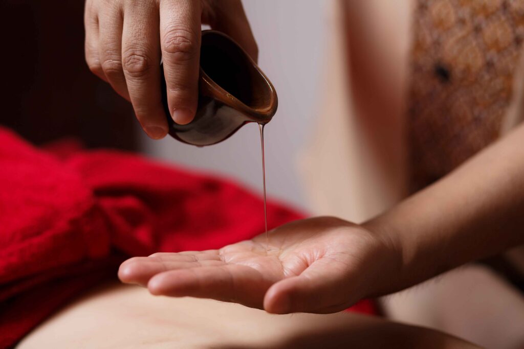 Masseur prepares to perform Thai massage treatment by placing aromatic oil on the client's back