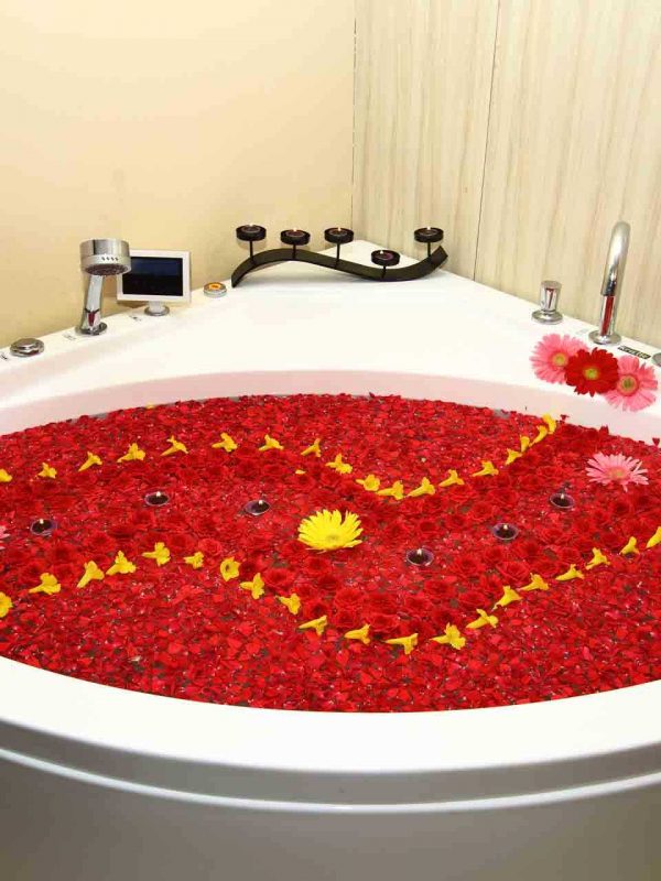 The Spa bath tub is decorated with an array of red fresh flowers and candles on water. Few candles and flowers surround it, as well as a small tablet