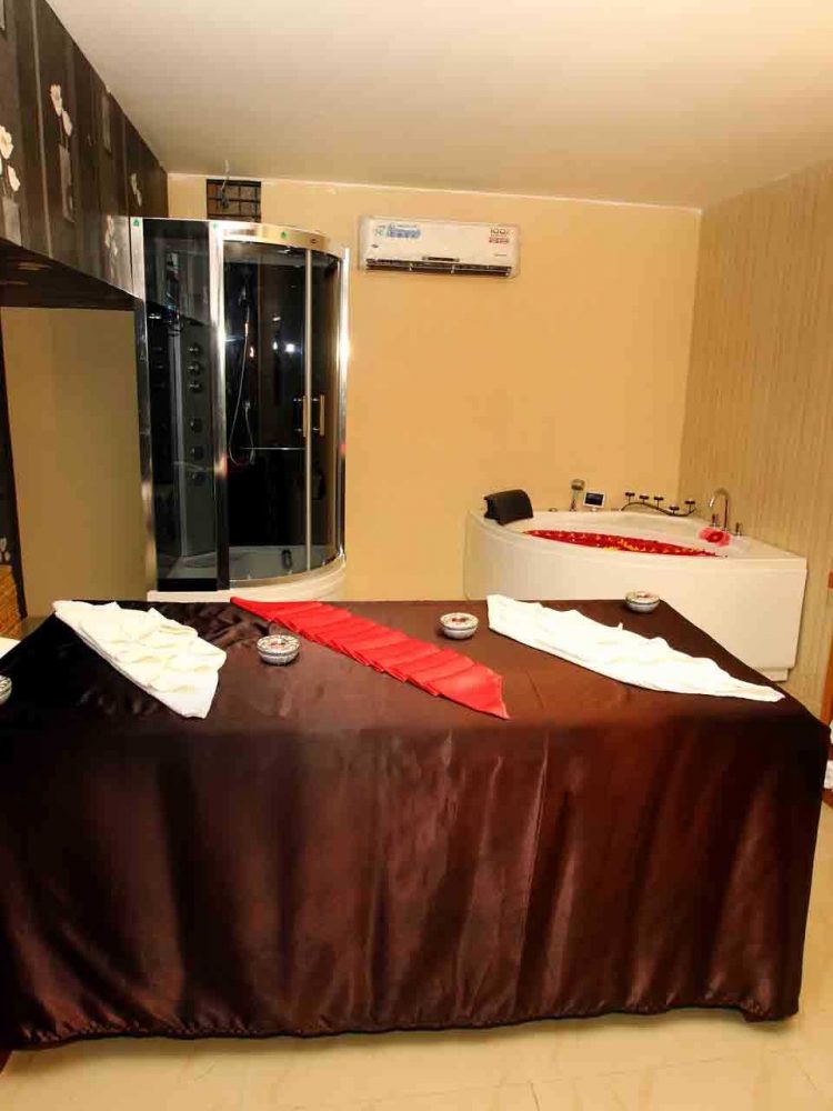 A side view of a fully air-conditioned room with a neatly decorated bed with aromatic candles. Beautifully decorated bathtubs and bath showers are provided inside the sports massage room at vellore for customer convenience.