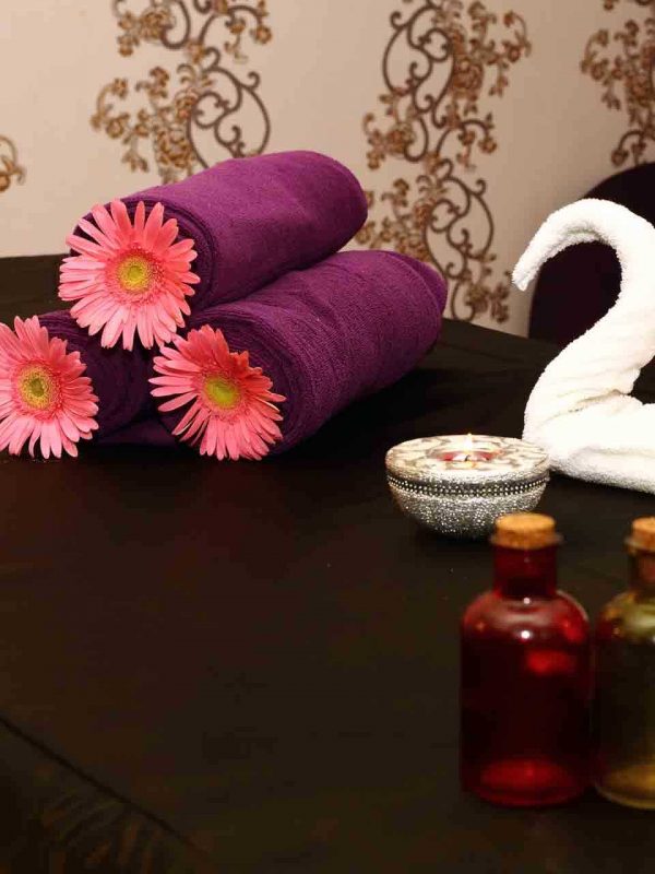Pleasant massage room with aromatic oil bottles, towels and bowl put up on a massage with black spread, all set up for Swedish massage in Vellore